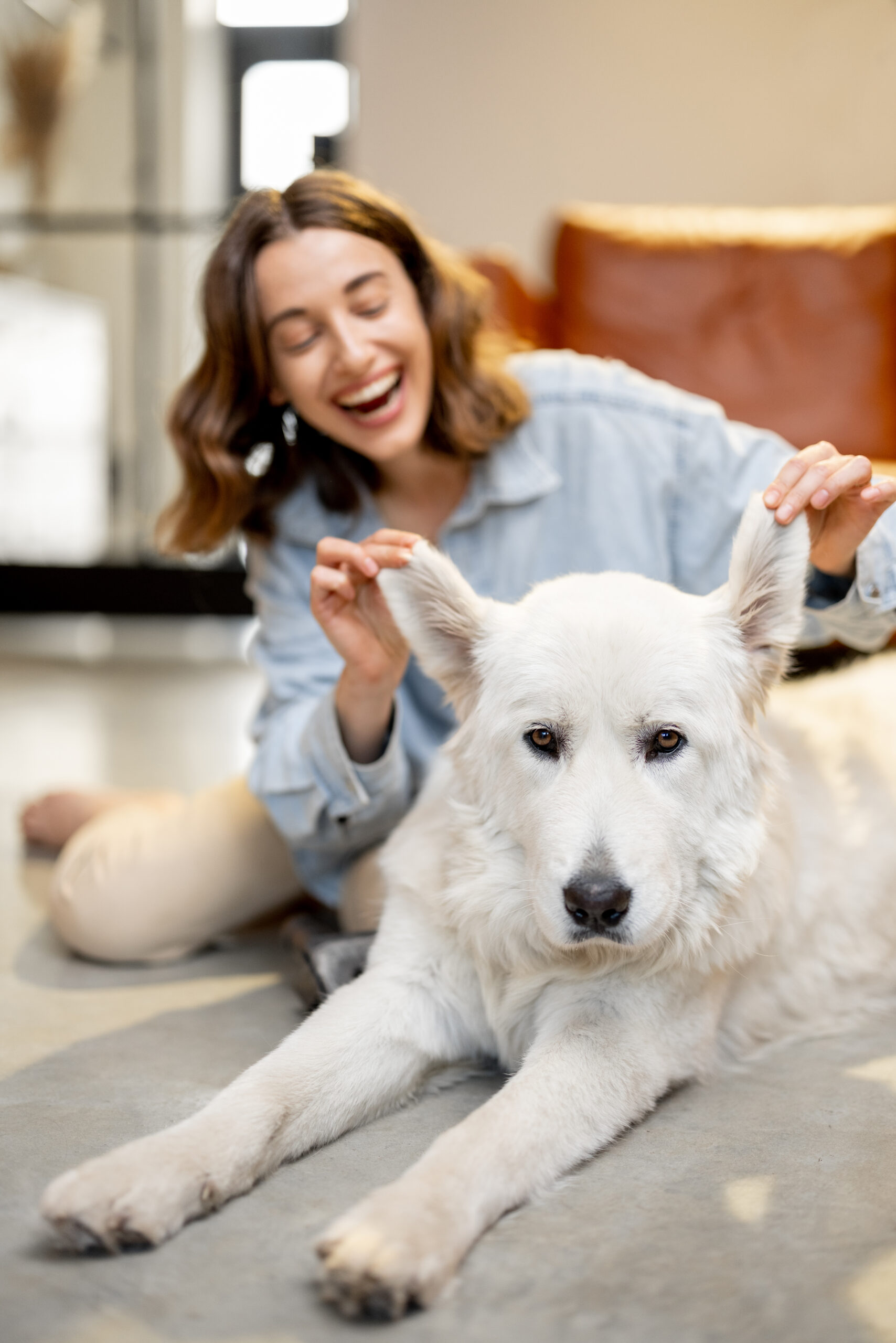 Portrait of a happy woman playing with her white cute dog on the floor at home